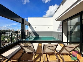 Terraço no telhado com piscina, espreguiçadeiras e vista para a cidade.