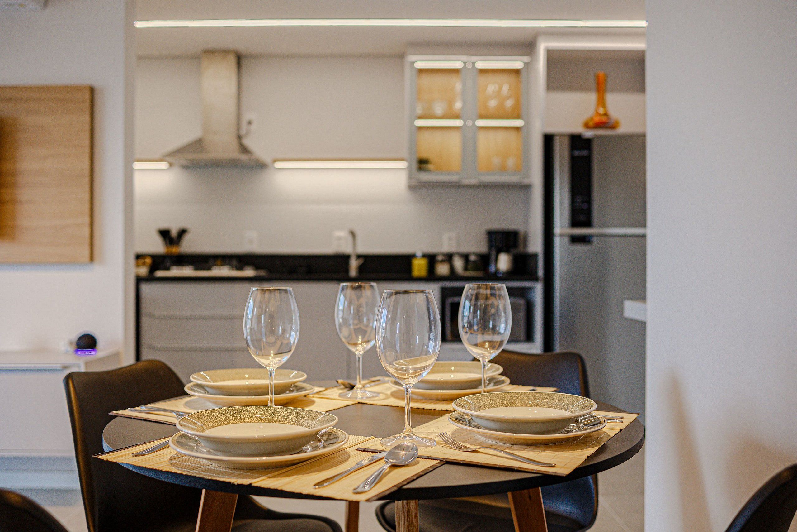 A dining table set with plates, cutlery, and wine glasses, with a modern kitchen in the background.