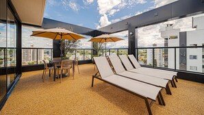 A rooftop terrace with lounge chairs, a table, and umbrellas. - Mingus Residencial Flipchave MIN000 (Joinville)