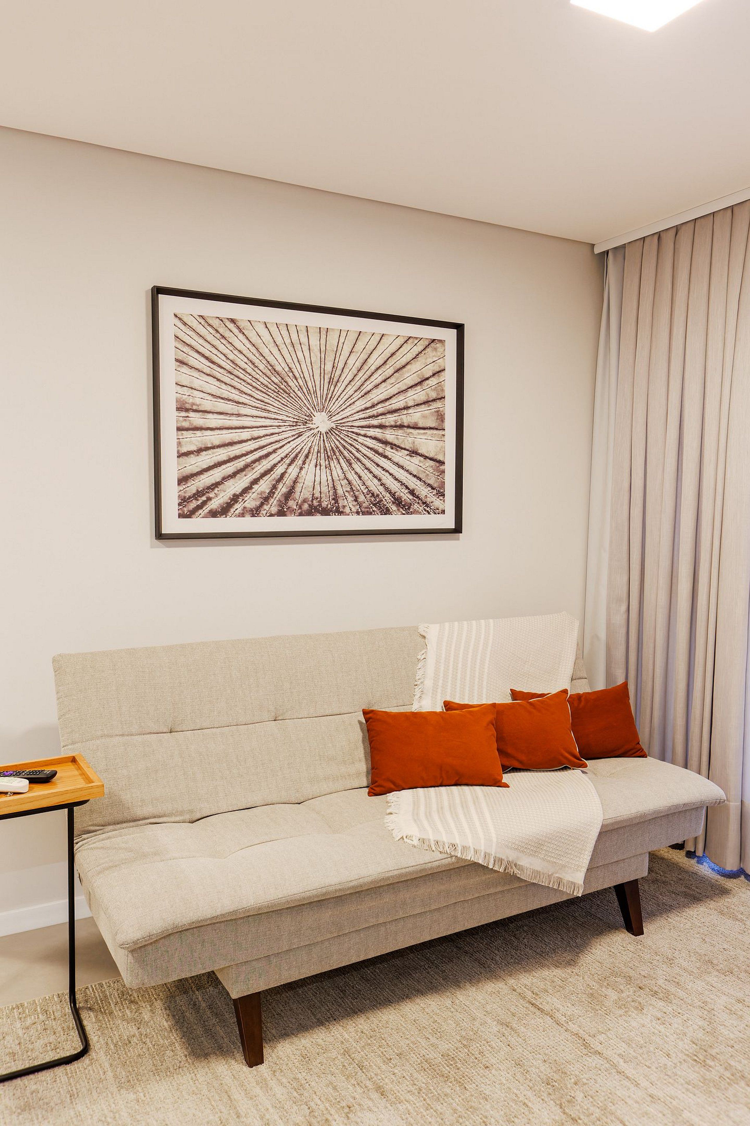 Una sala de estar con un sofá, una obra de arte enmarcada y una ventana con cortinas.