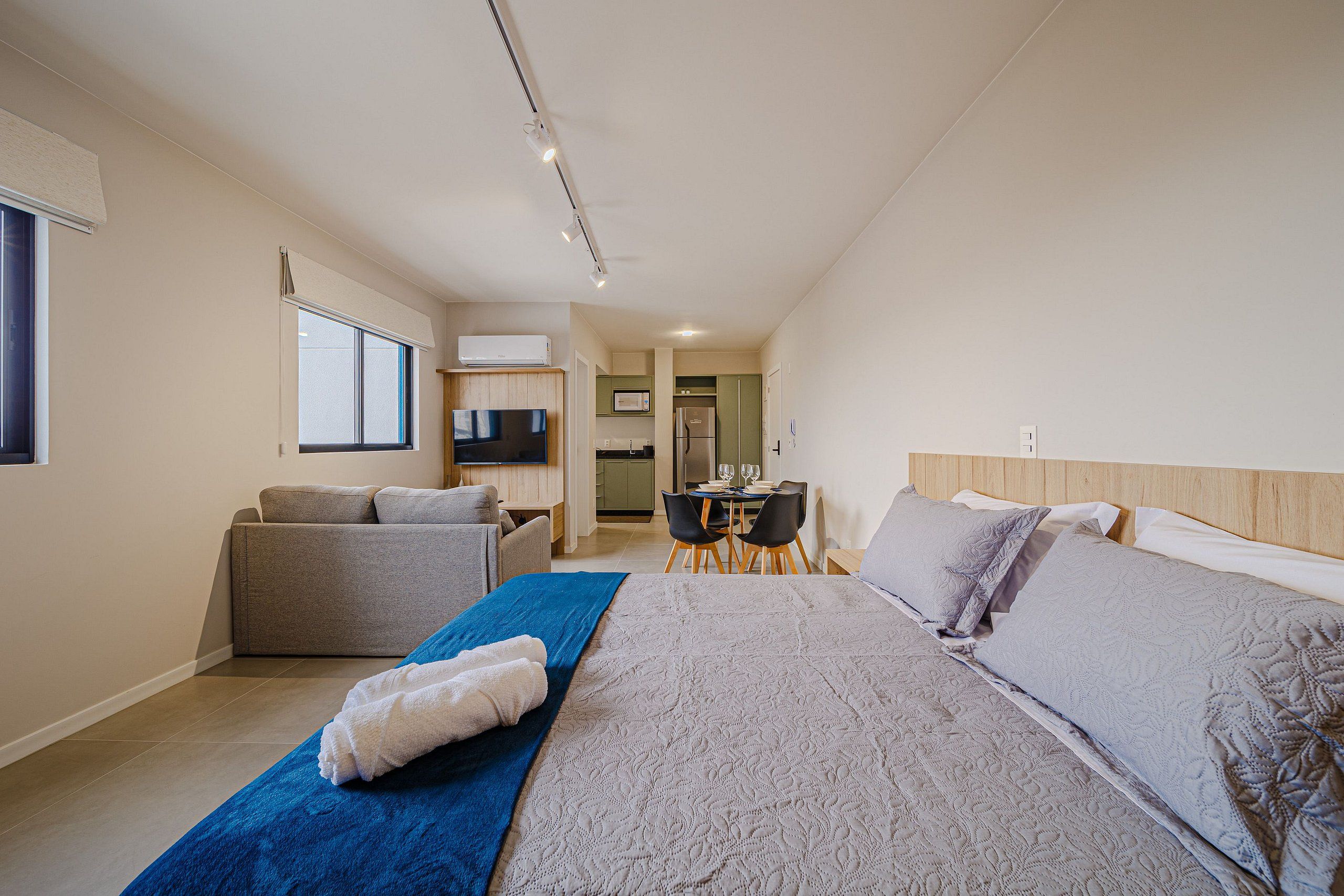 A bedroom with a bed, a sofa, a dining table, and a kitchen area.