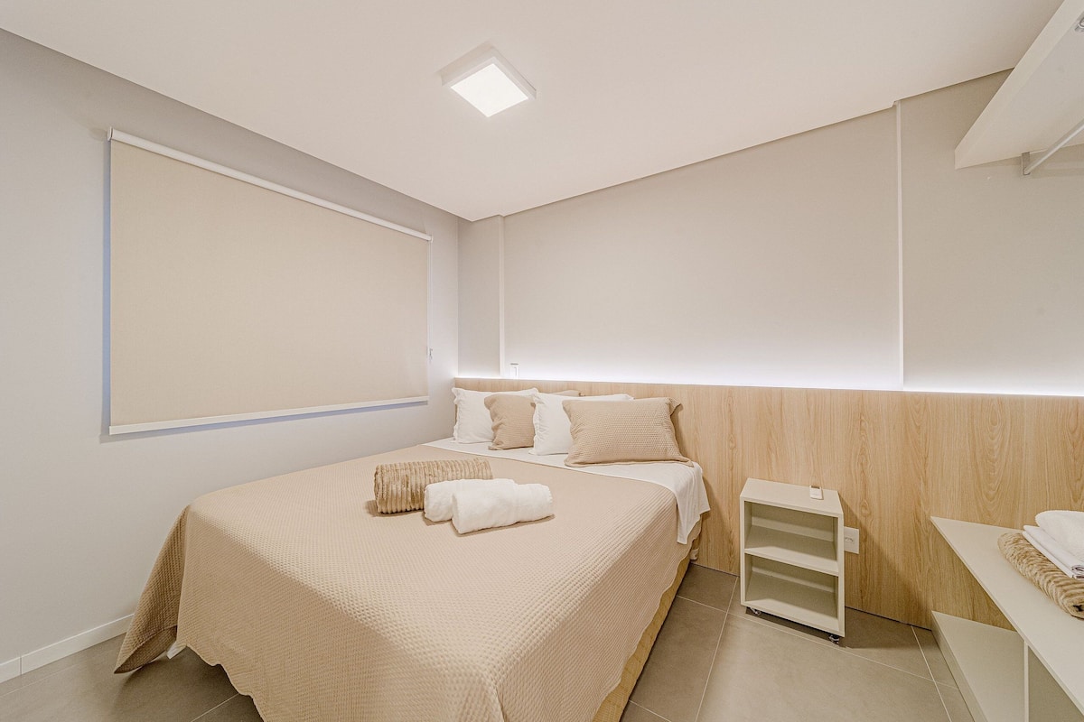 Une chambre d’hôtel moderne, dotée d’un grand lit, d’une table de chevet, d’une étagère intégrée et d’une grande fenêtre.