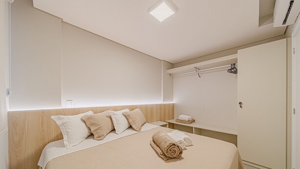 Een hotelkamer met een bed, nachtkastje, handdoek, kledingkast en een plafondlamp.