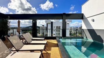 A rooftop pool area with sun loungers and a view of the city.