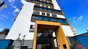 Een meerlaags gebouw met een modern architectonisch ontwerp, met een opvallende entree met een glazen deur en een bord waarop 'MINGUS 897' staat.