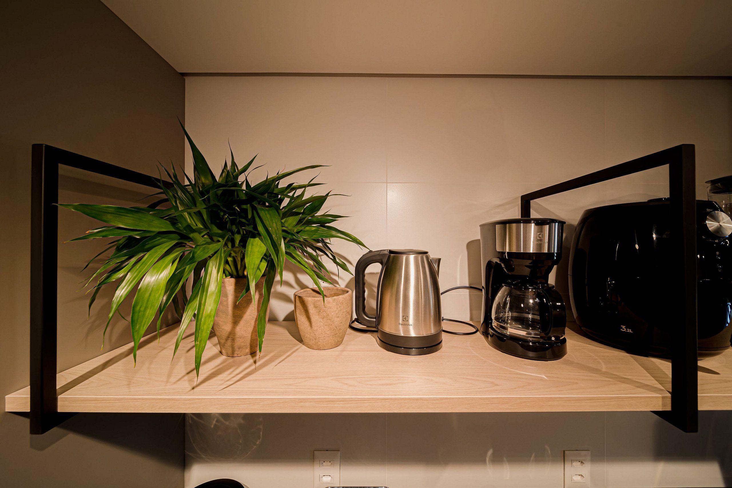 Una encimera de cocina con cafetera, hervidor, planta y jarra de café.