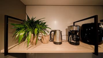 Una encimera de cocina con cafetera, hervidor, planta y jarra de café.