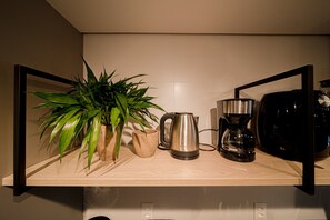 Un plan de travail de cuisine avec une machine à café, une bouilloire, une plante et une cafetière.