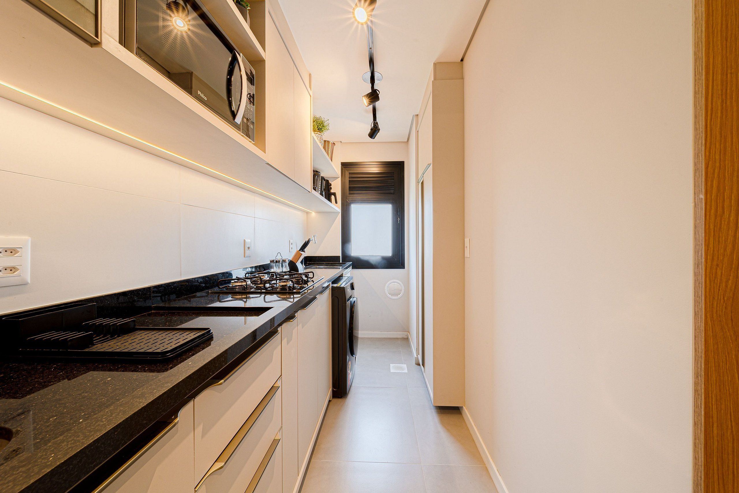 A narrow kitchen with a black countertop, white cabinets, and a window at the end.