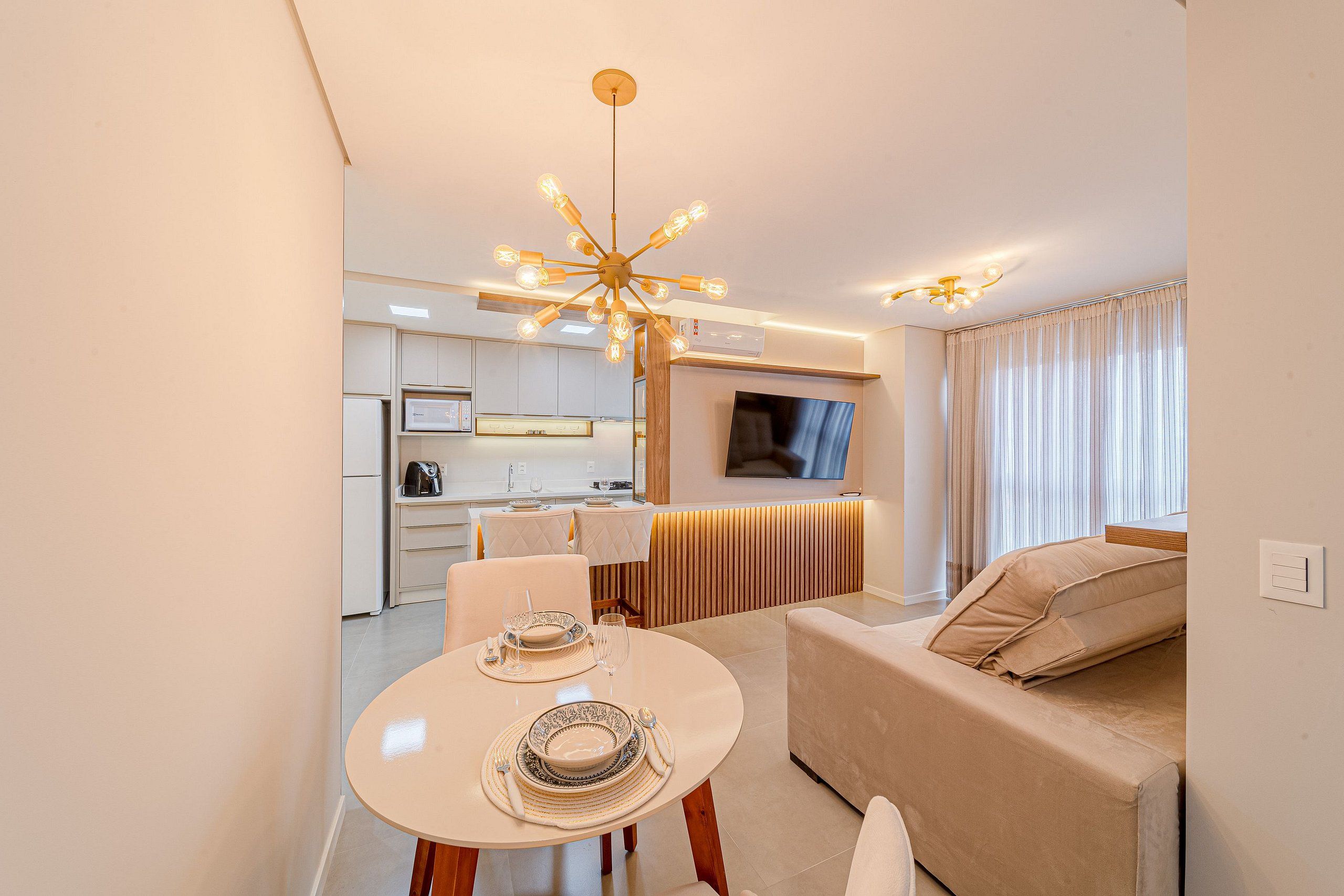 A modern living room with a dining area, a sofa, a TV, and a kitchen in the background.