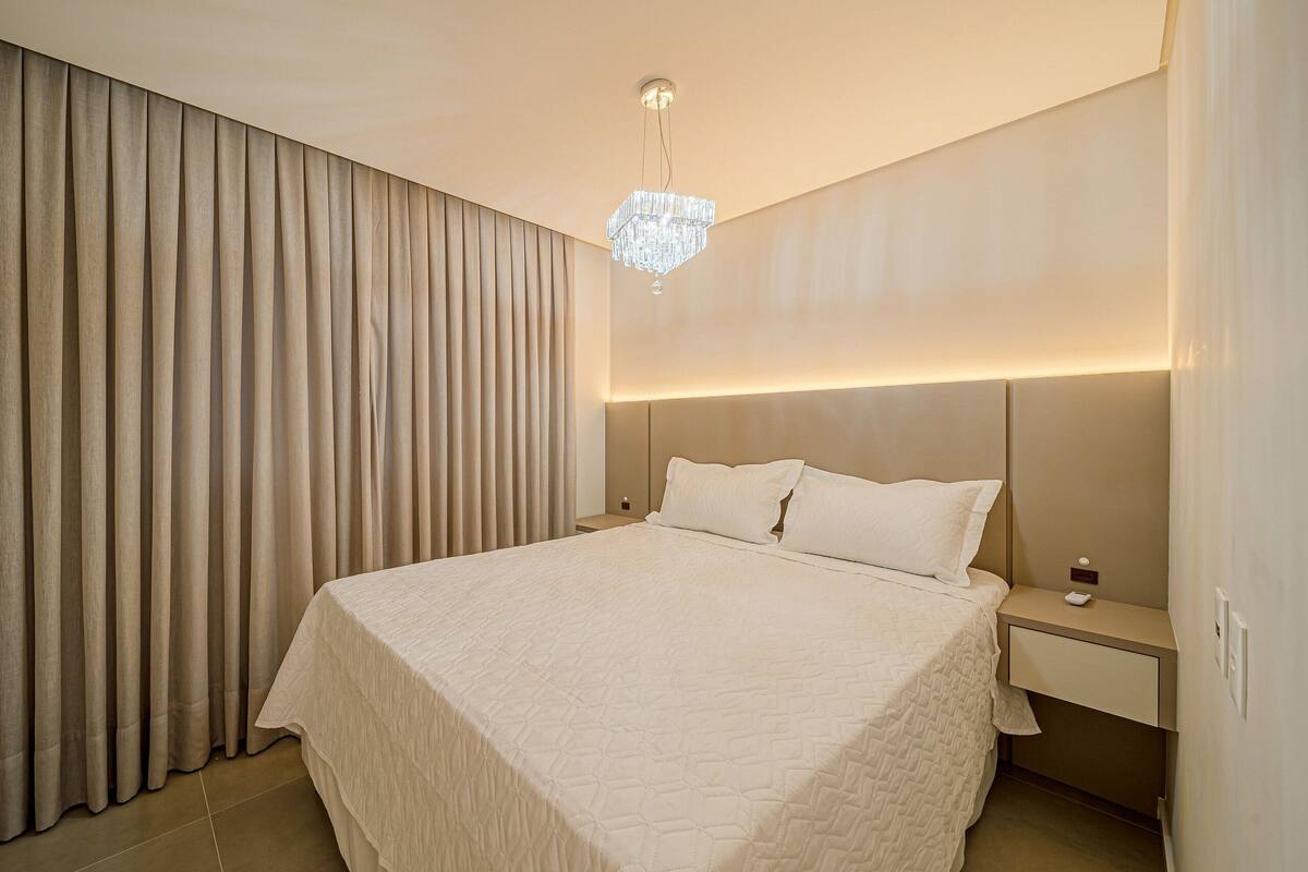 Une chambre d’hôtel avec un grand lit, une table de chevet, une lampe fixée au mur et une fenêtre avec des rideaux.