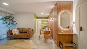 Een moderne woonkamer met een bruine leren bank, een eettafel met stoelen, een houten kaptafel met spiegel en een klein houten krukje.