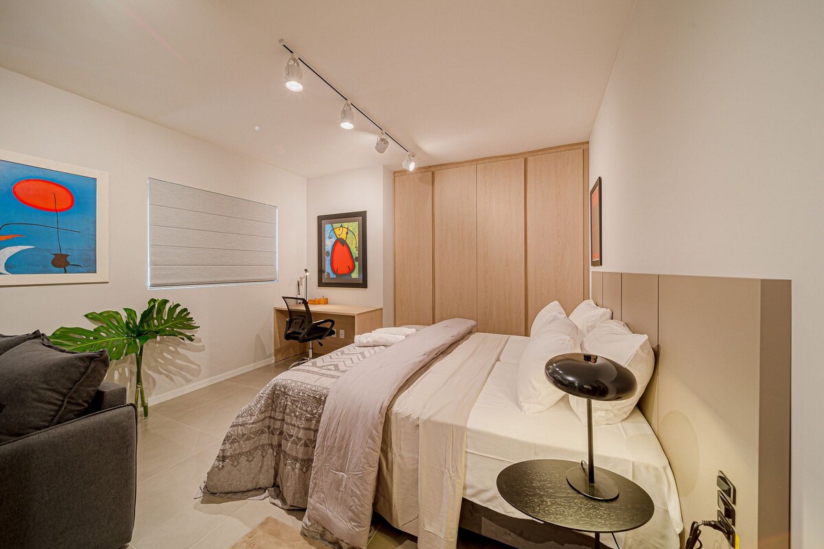 A bedroom with a bed, bedside table, lamp, chair, and artwork on the walls.