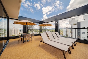 Une terrasse sur le toit, avec des chaises longues, une table et des parasols.