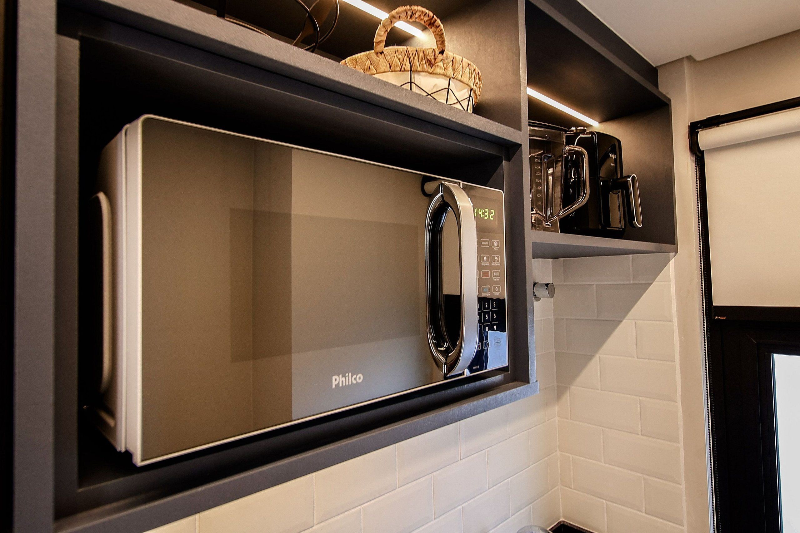 A kitchen with a built-in microwave, a coffee machine, and a basket on the shelf.