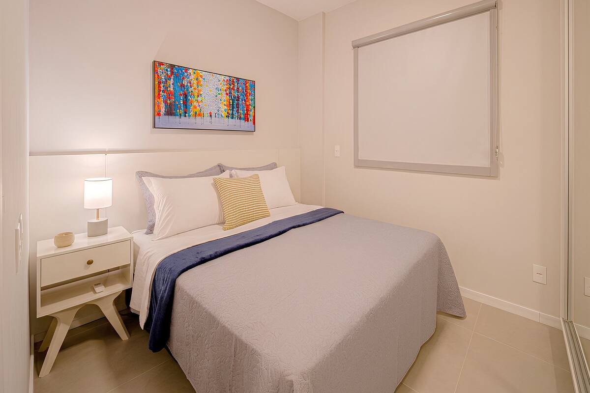Une chambre à coucher avec un lit, une table de chevet, une lampe et un tableau abstrait aux couleurs vives accroché au mur.