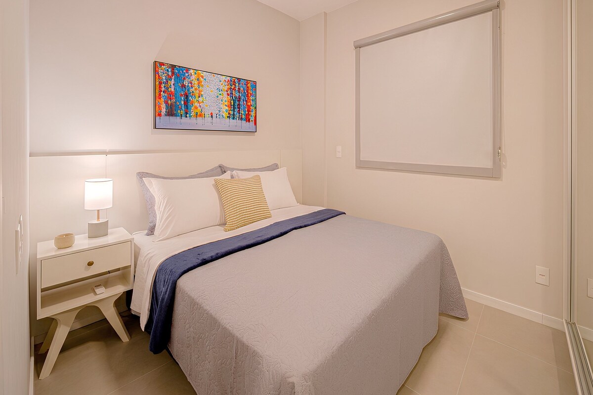 A bedroom with a bed, nightstand, lamp, and a colorful abstract painting on the wall.