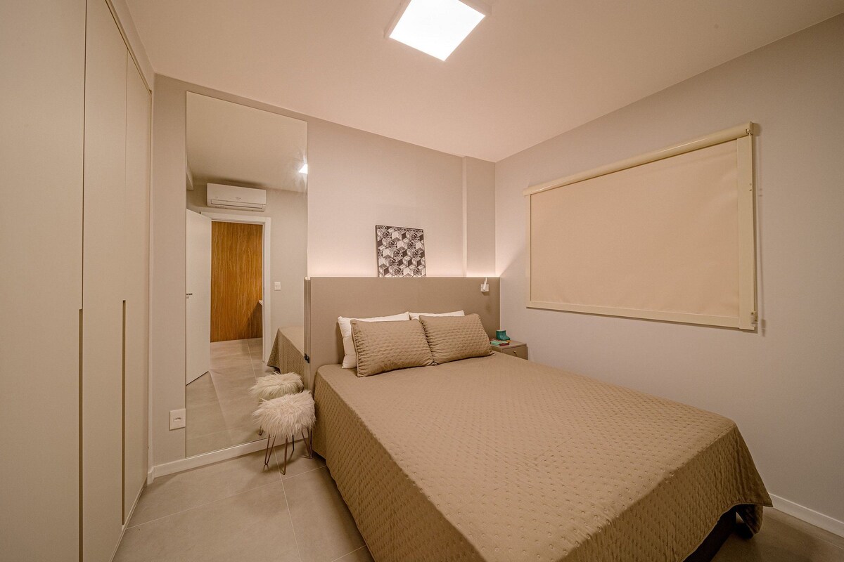 A bedroom with a bed, a nightstand, a mirror, and a door leading to another room.