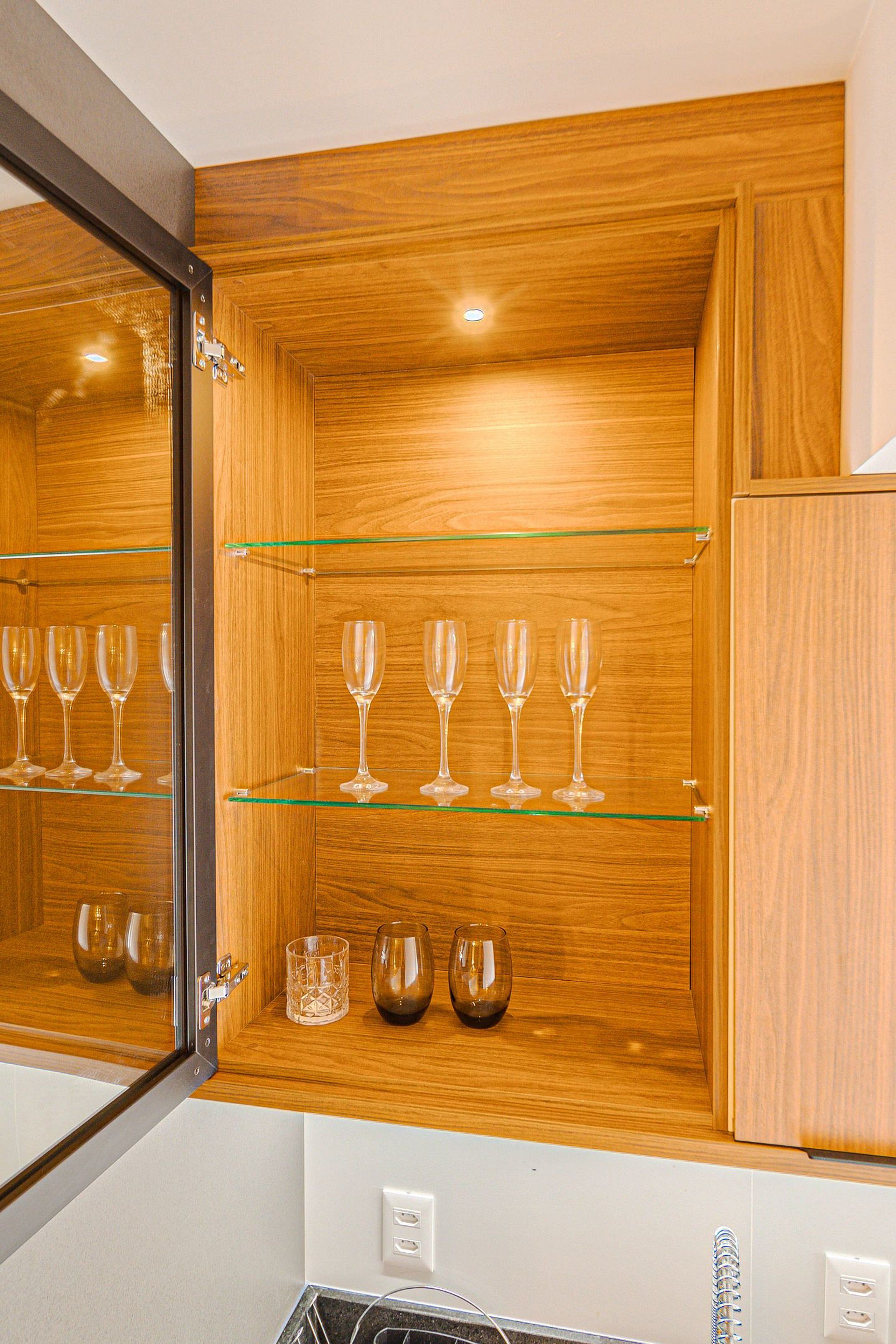 Un aparador de madera con estantes de vidrio que contiene copas de vino y un vaso.