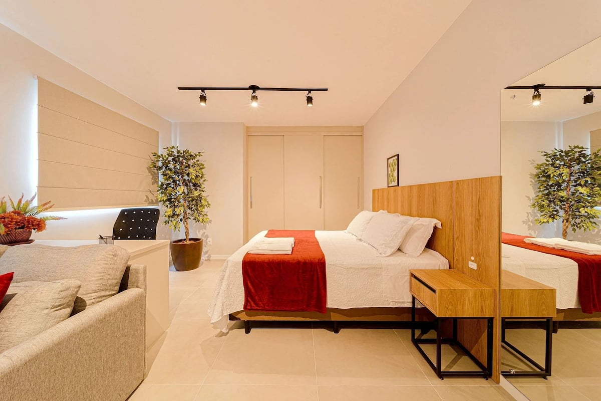 Une chambre d’hôtel moderne comprenant un lit, une table de chevet en bois, un canapé, un bureau et un miroir.