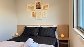 A neatly made bed with a quilted cover, a bedside table with a lamp, and a wall with framed artwork. - Mingus Residencial Flipchave MIN000 (Joinville)