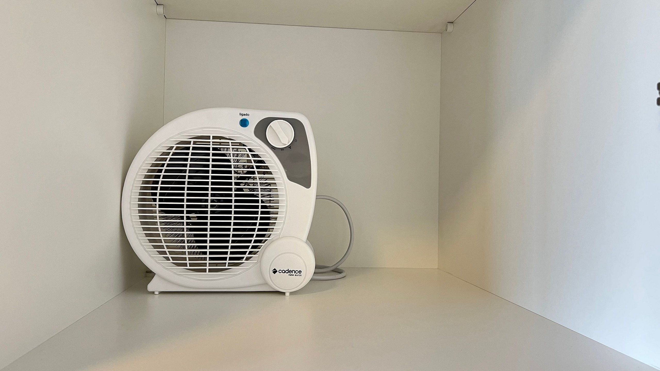 A white fan with a control panel and a cord, placed in a corner of a room with plain walls.