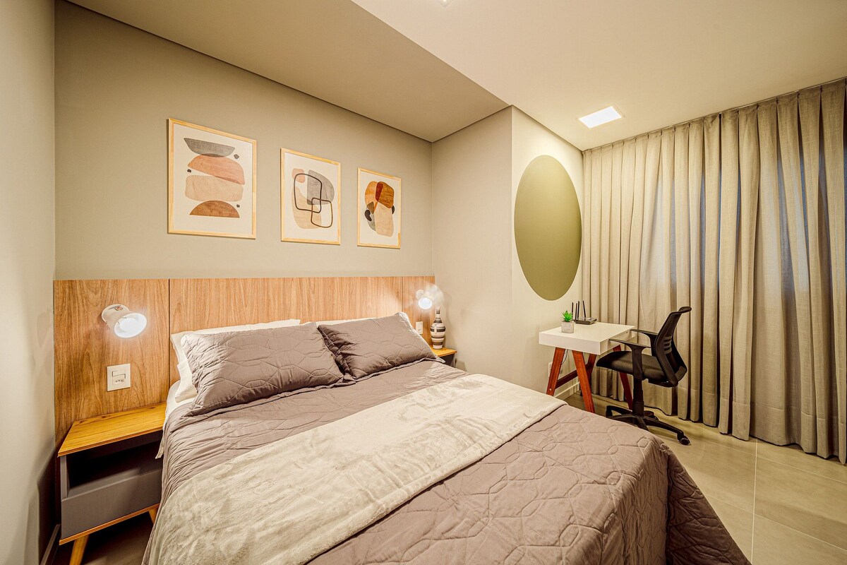 A bedroom with a bed, bedside tables, a desk, a chair, and artwork on the wall.