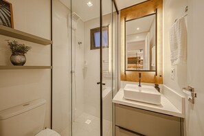 Un baño moderno con cabina de ducha de vidrio, un lavabo blanco y un espejo con marco de madera.