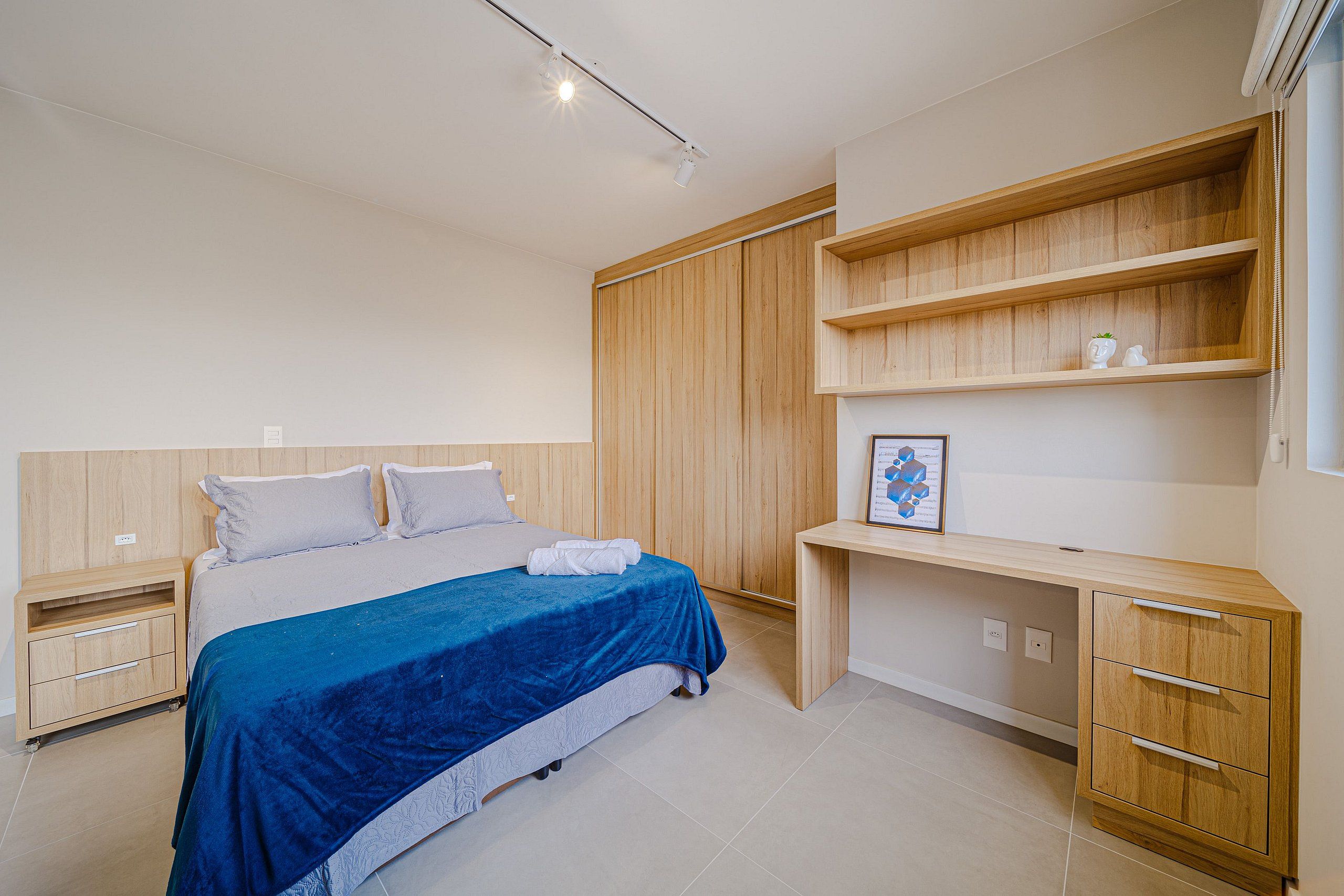 Un dormitorio con cama, mesitas de noche, escritorio y estanterías empotradas.