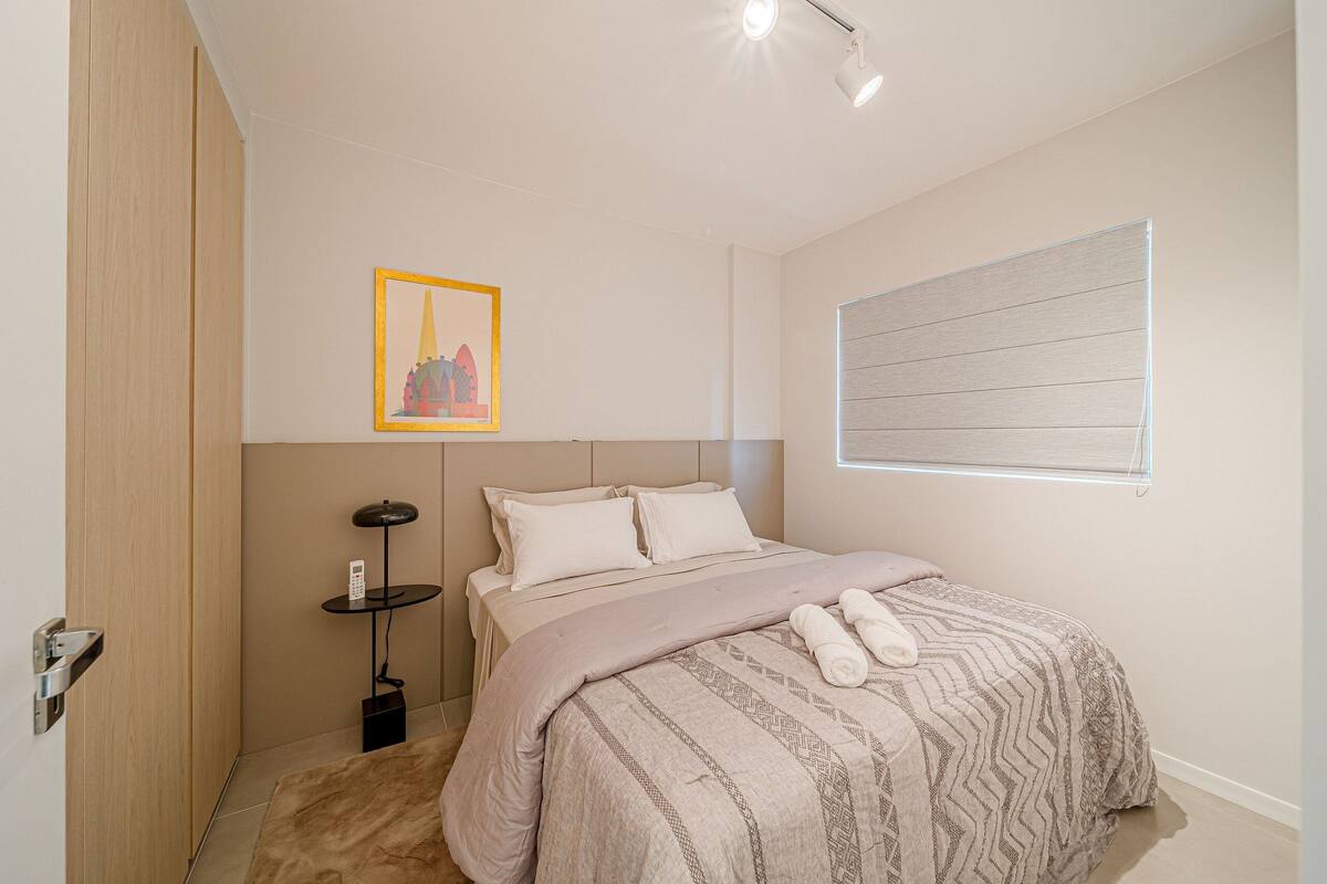 Une chambre à coucher avec un lit, une table de chevet, une lampe et un tableau encadré au mur.