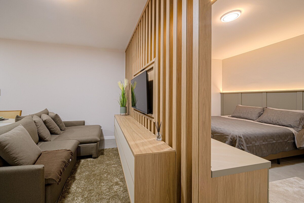 A modern hotel room with a sofa, a TV, a bed, and a wooden partition.