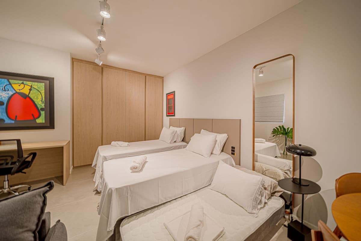 Une chambre d’hôtel avec deux lits, un bureau, une chaise, un miroir et un tableau au mur.