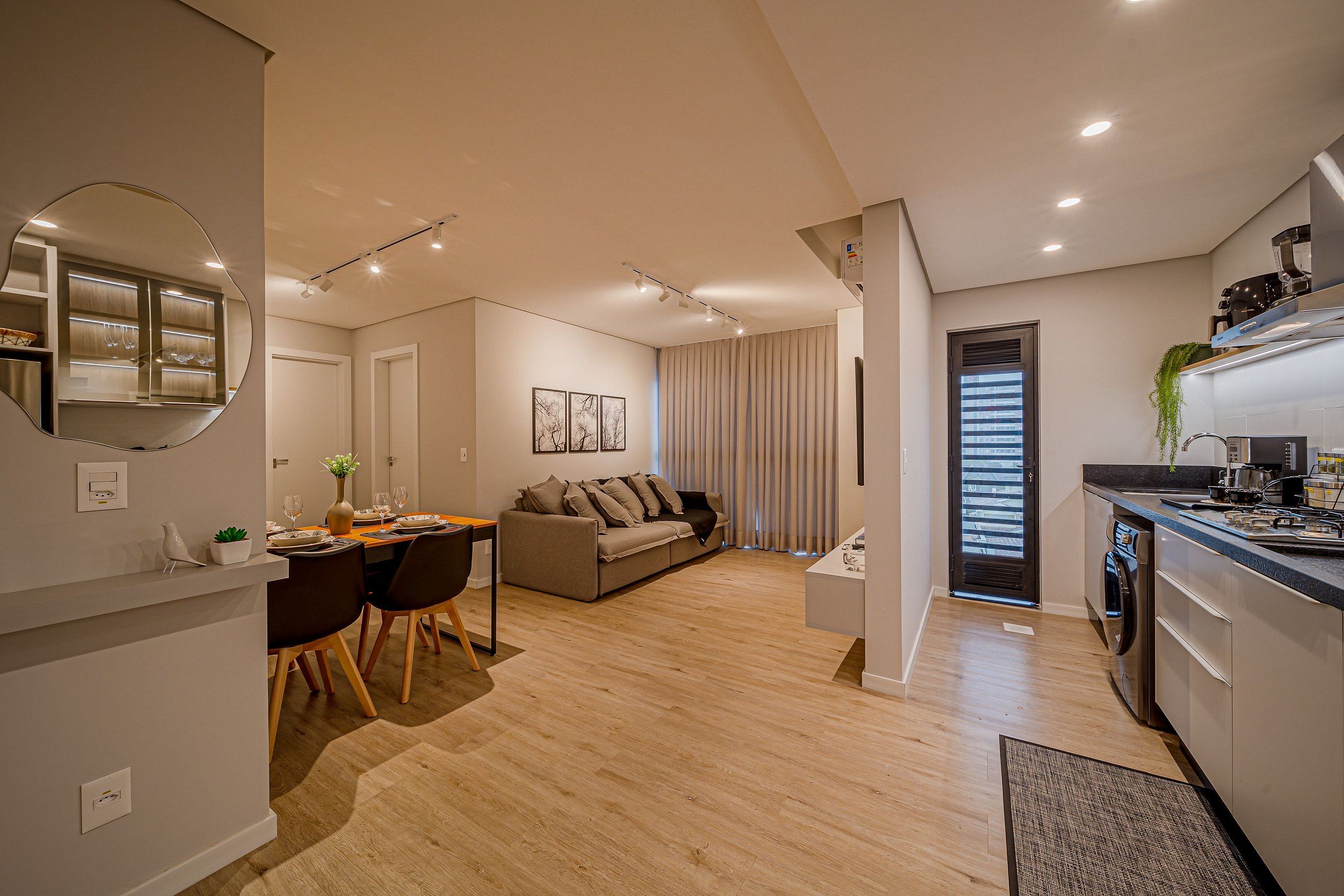 A modern apartment with a dining area, sofa, kitchen, and a large mirror.
