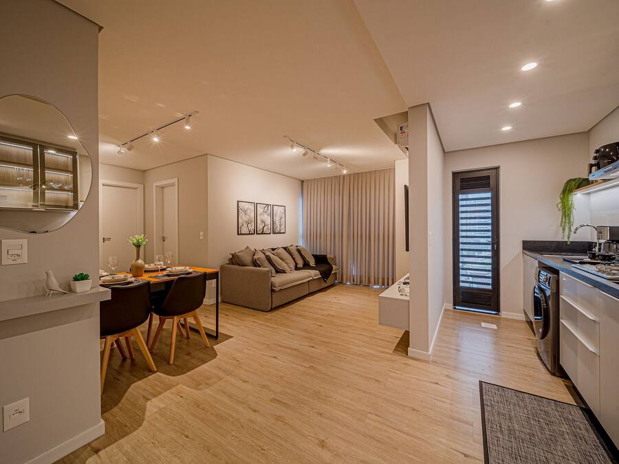 A modern apartment with a dining area, sofa, kitchen, and a large mirror.