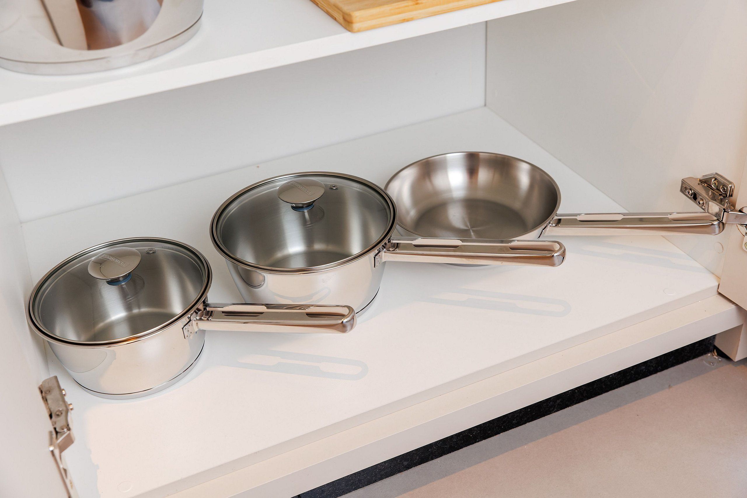 Stainless steel cookware on a white shelf.