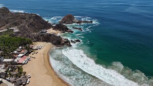 A coastal area with a sandy beach, rocky outcrops, and a small resort with thatched-roof buildings and umbrellas. - Hotel Estrella de Mar (San Pedro Pochutla)