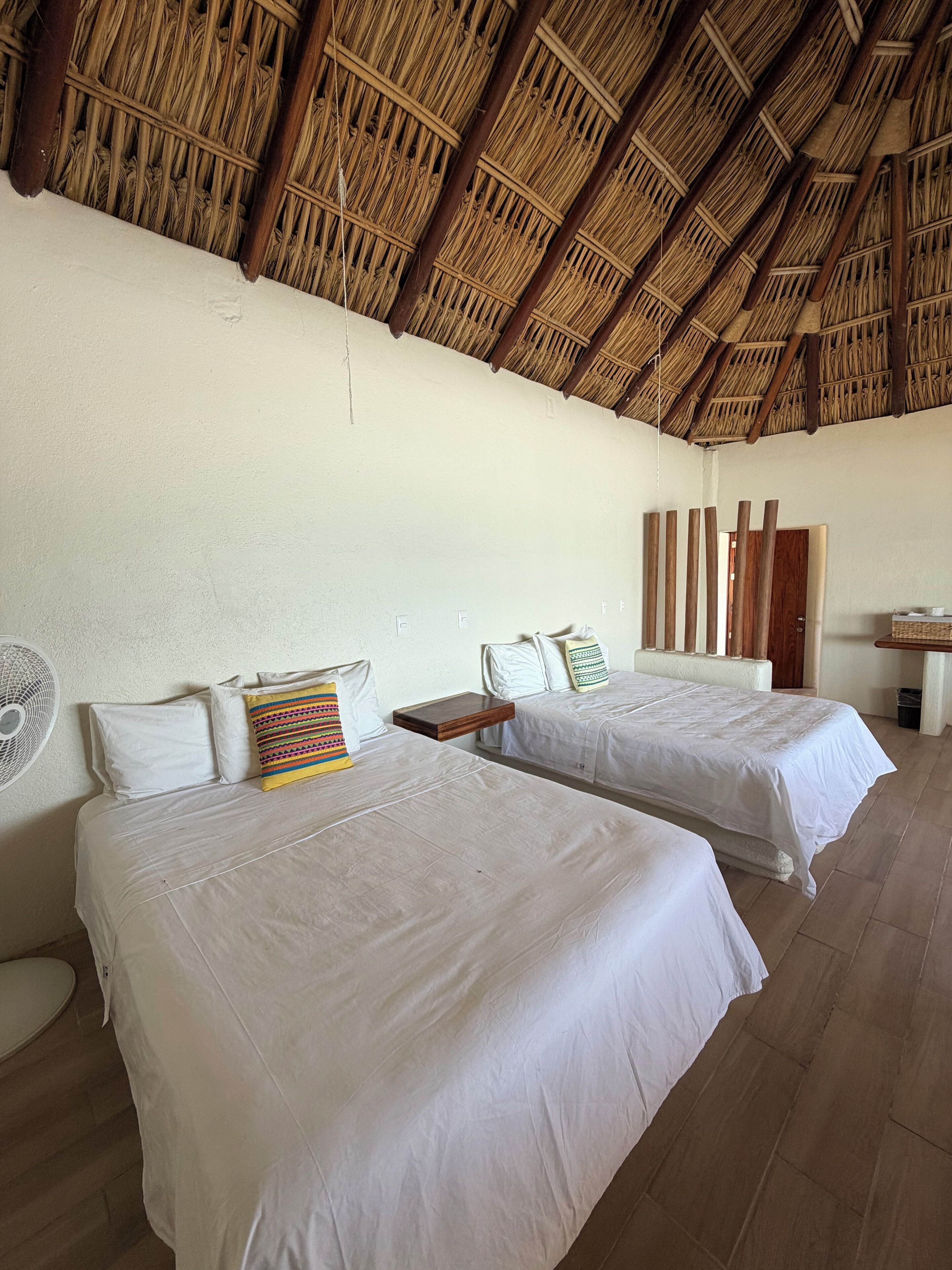 Una habitación con dos camas, un ventilador y techo de paja.