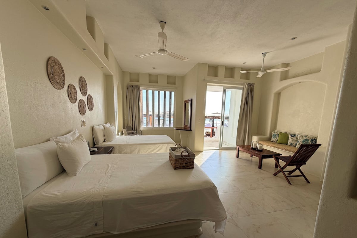 Habitación de hotel con dos camas, un sofá, una silla, una mesa y un balcón con cortinas.