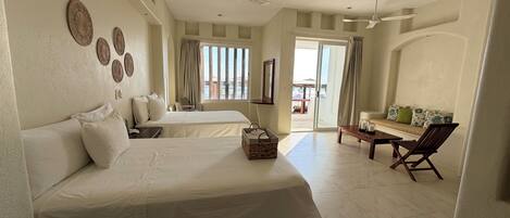 A hotel room with two beds, a sofa, a chair, a table, and a balcony with curtains.