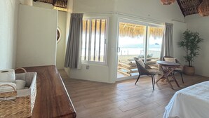 A spacious room with a high ceiling, wooden flooring, a large window with curtains, wicker furniture, and a view of the beach. - Hotel Estrella de Mar (San Pedro Pochutla)