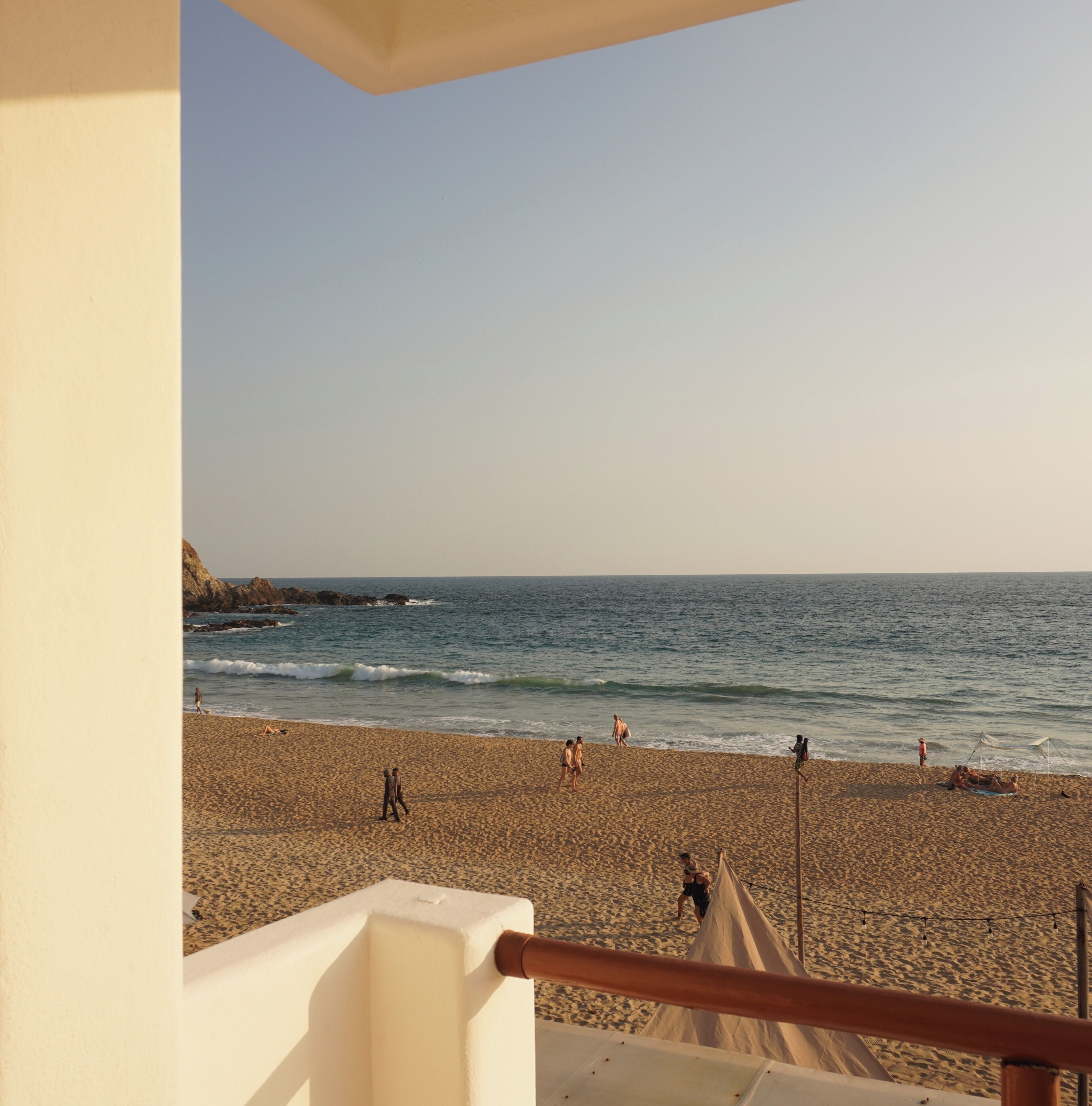 A beach view from a balcony with a railing, sandy beach, and ocean.