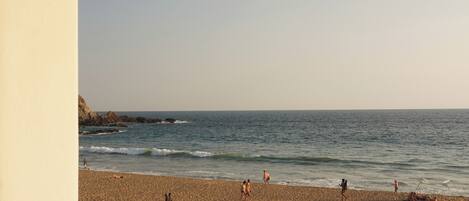 A beach view from a balcony with a railing, sandy beach, and ocean.