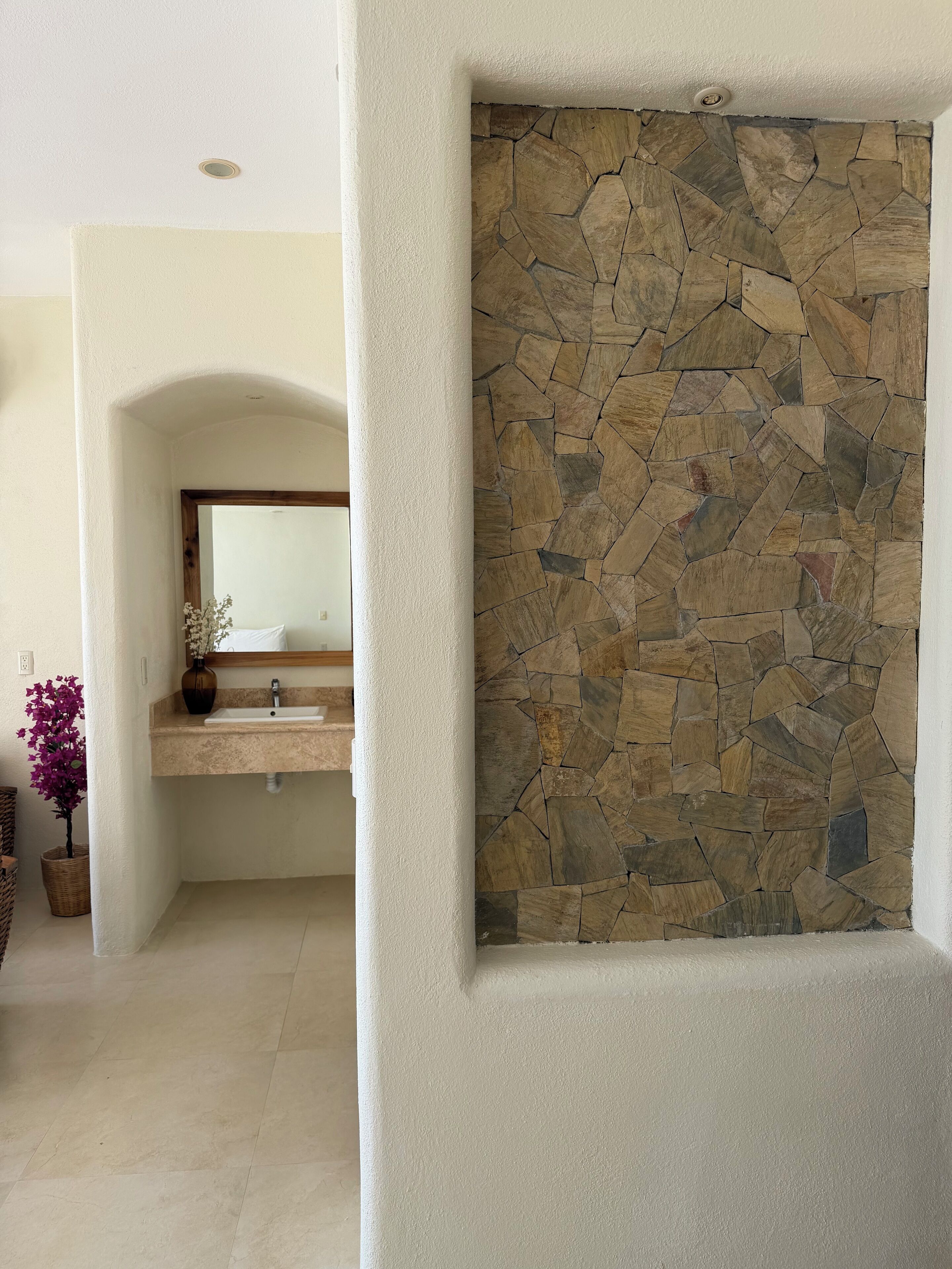 A bathroom with a stone wall, a sink with a mirror, and a potted plant.