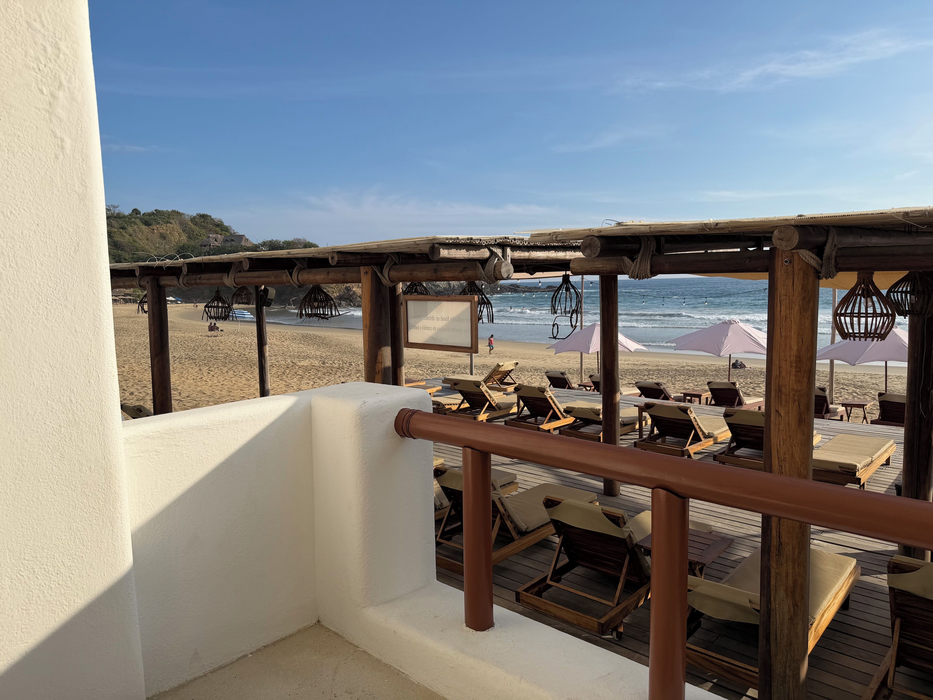 A wooden deck with lounge chairs and umbrellas overlooking a beach.