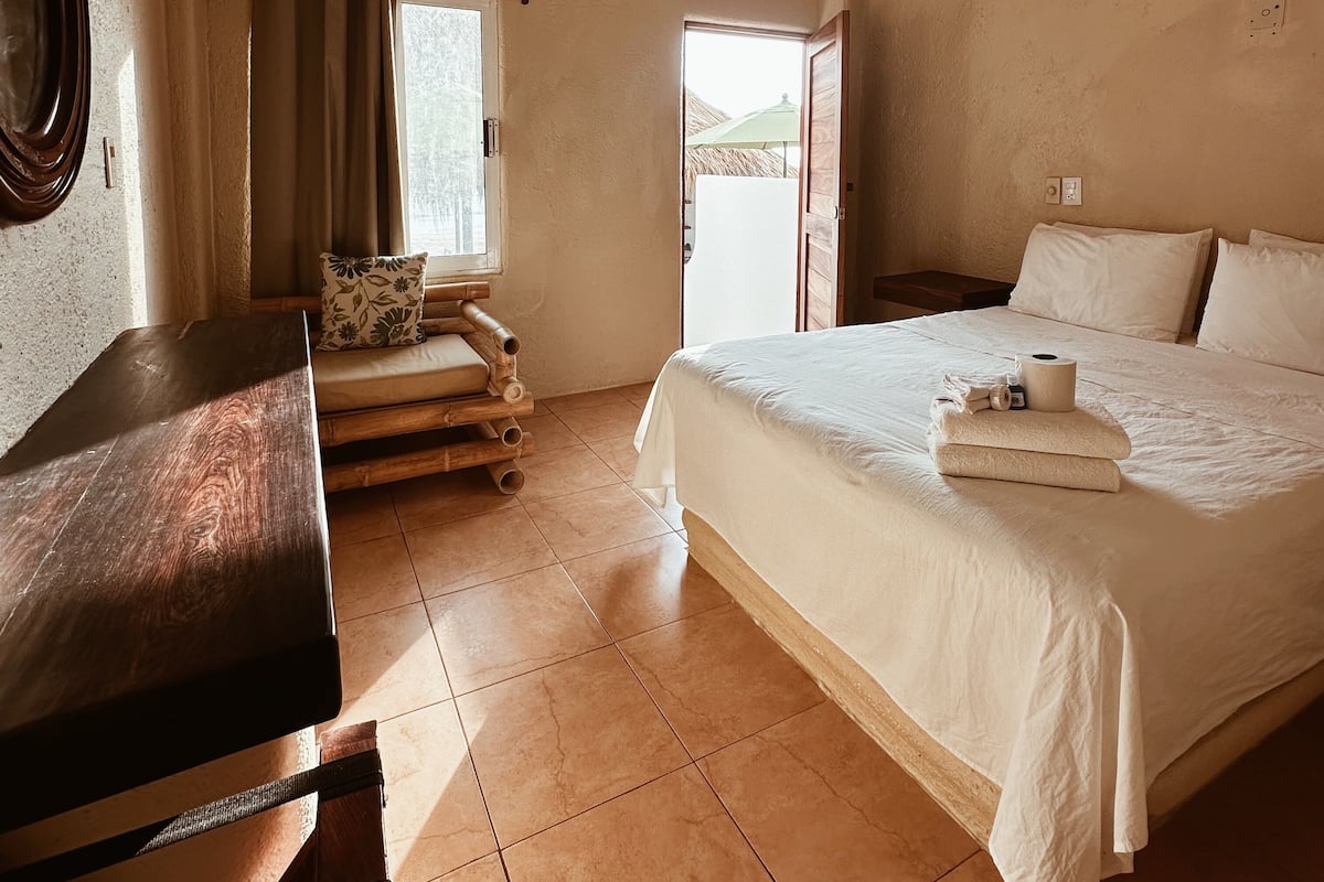 Un dormitorio con cama, escritorio, ventilador de techo y ventana con cortinas.