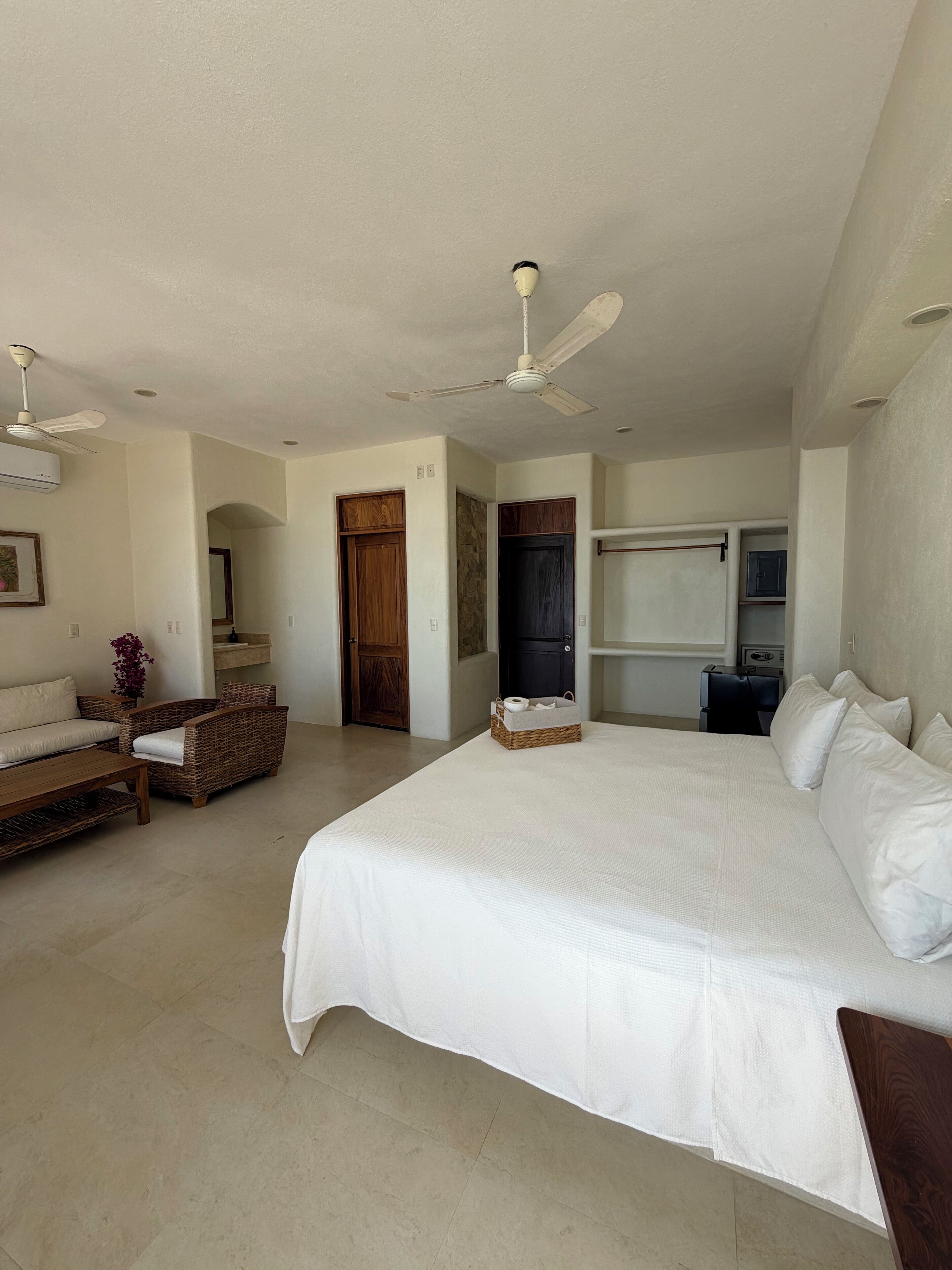 A spacious bedroom with a large bed, a ceiling fan, a television, and a wicker sofa.