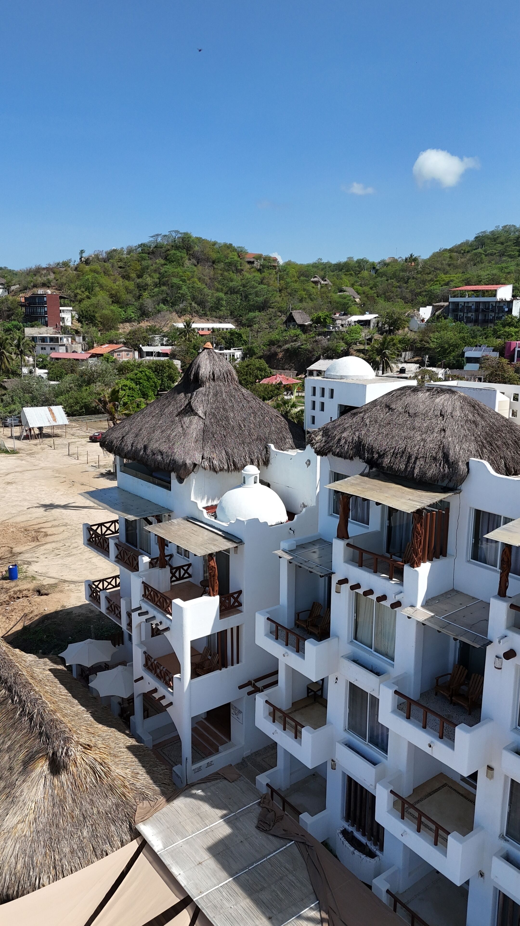A resort with white buildings, thatched-roof structures, and a beach view.