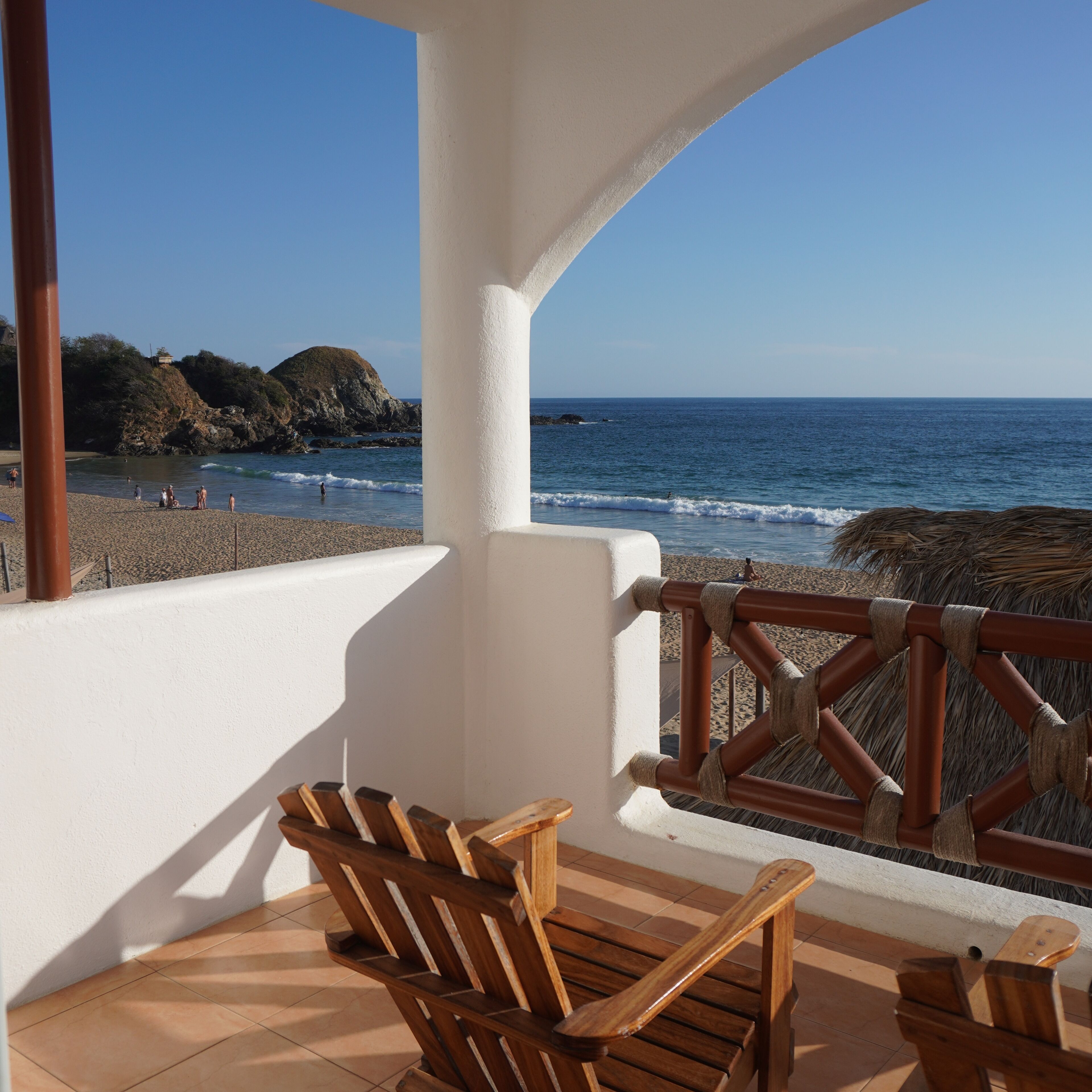 A wooden deck with chairs overlooking a beach and ocean.