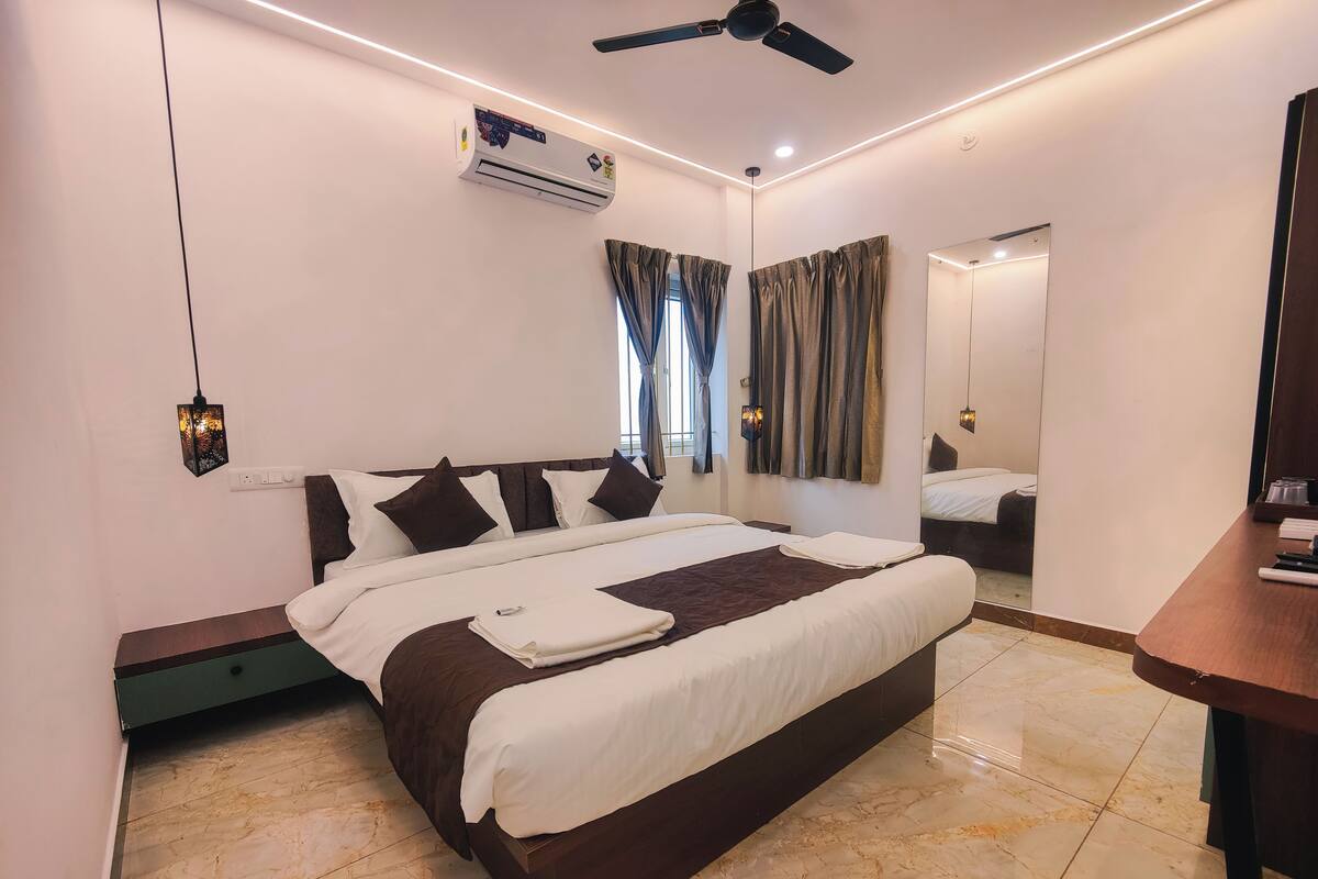 A modern hotel room with a large bed, an air conditioning unit, a ceiling fan, and a mirror.