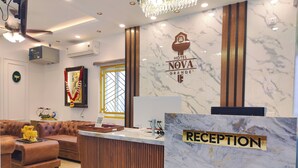 A hotel reception area with a marble reception desk, a brown leather sofa, and a chandelier. - Nova Grande' (Hosur)